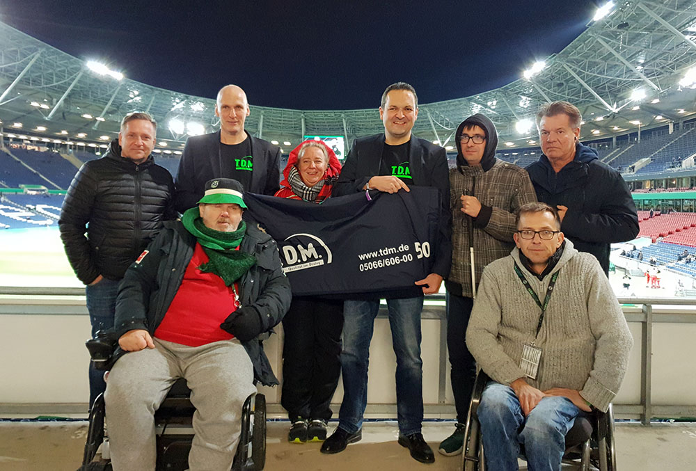 Bildunterschrift: Warm eingepackt (v.l.n.r.): 96-Manager Horst Heldt, stellv. Sprecher d. Arbeitskreis Barrierefreies Stadion Frank Hepe, T.D.M.-Geschäftsführer Dietmar Klug, Sprecherin d. Arbeitskreis Barrierefreies Stadion 96 Hendrikje Rothkegel, kaufm. Leiter von T.D.M. Martin Knopp, Hannover 96 Fan Tobias Gehrke, 96-Behindertenfanbeauftragter Detlef Kühne und Stadionchef Thorsten Meier. © Hannover 96